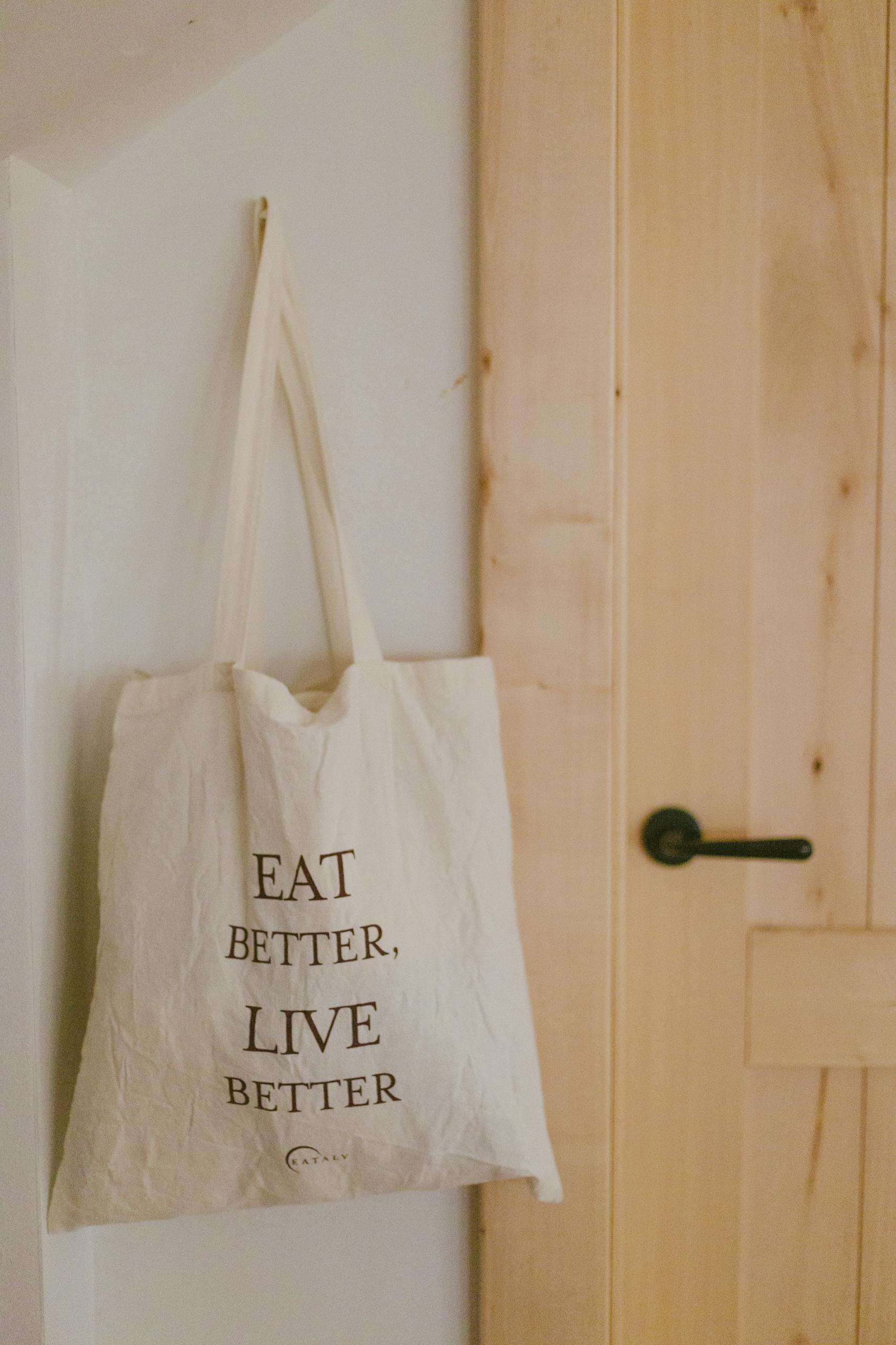 Tote bag with 'Eat Better, Live Better' quote hanging on wooden door.